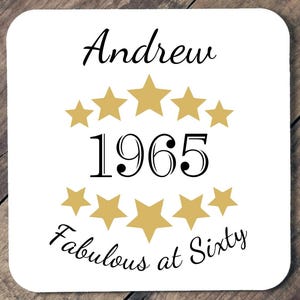 Può includere: Sottobicchiere quadrato bianco con il nome "Andrew" in corsivo nero sopra l'anno "1965" in nero, circondato da stelle dorate. La frase "Fabulous at Sixty" è scritta in nero sotto.