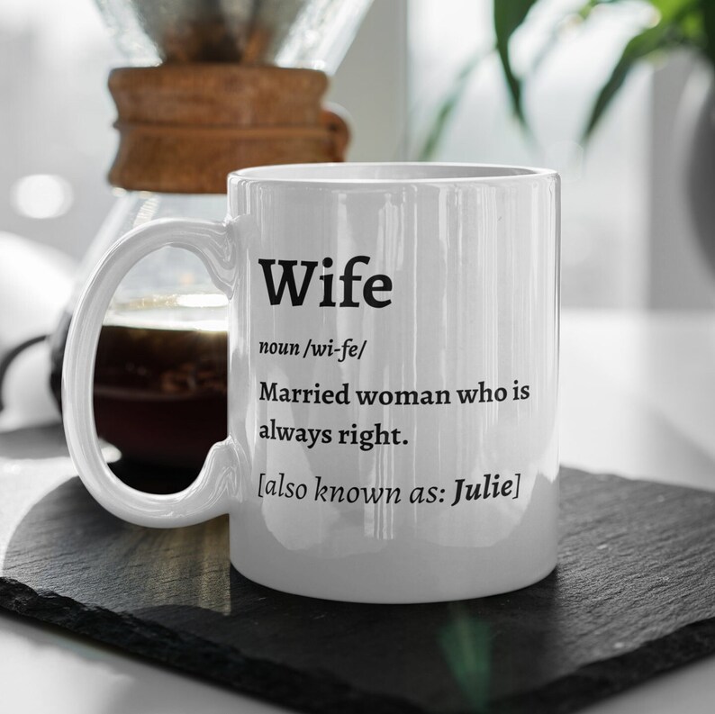 May include: White ceramic mug with the definition of "Wife" printed in black. The definition includes the pronunciation, a description, and "also known as: Julie."