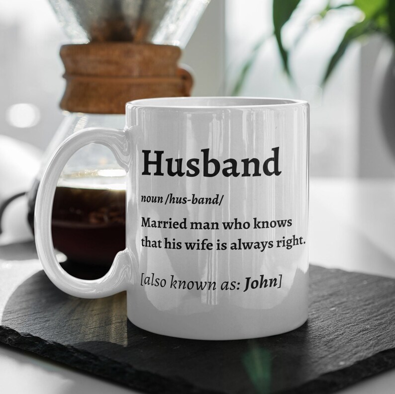May include: White ceramic mug with the definition of "Husband" printed in black. The definition includes the phrase "Married man who knows that his wife is always right." The mug also states "also known as: John."