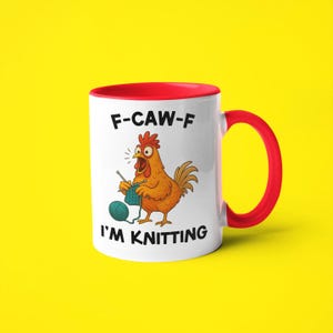 May include: White ceramic mug with a red interior and handle. The mug features a cartoon chicken knitting with the text "F-CAW-F" above and "I'M KNITTING" below the chicken. The background is yellow.