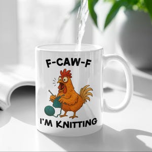 May include: White ceramic mug featuring a cartoon chicken knitting with the text "F-CAW-F I'M KNITTING". The chicken is orange with a red comb and is knitting with blue yarn. The mug has a curved handle.