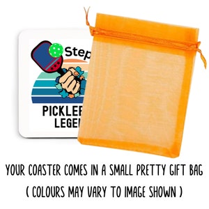 May include: A white square coaster with a pickleball paddle and ball design, the text "PICKLEBALL LEGEND" is printed on the coaster. The coaster is packaged in an orange gift bag.