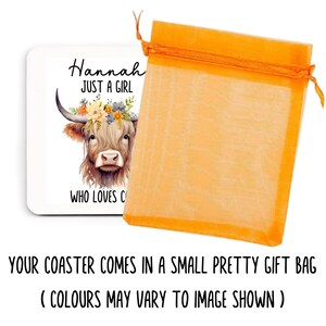 May include: A white square coaster featuring a watercolor illustration of a Highland cow wearing a floral crown. Text reads "Hannah JUST A GIRL WHO LOVES C". The coaster is next to an orange gift bag.