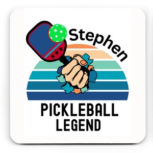 May include: White square coaster with a graphic of a pickleball paddle and ball, a fist breaking through a striped background, and the text "Stephen" and "Pickleball Legend."