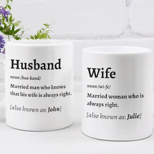 May include: Two white ceramic mugs with black text. One mug says "Husband" with a definition and "also known as: John." The other mug says "Wife" with a definition and "also known as: Julie."