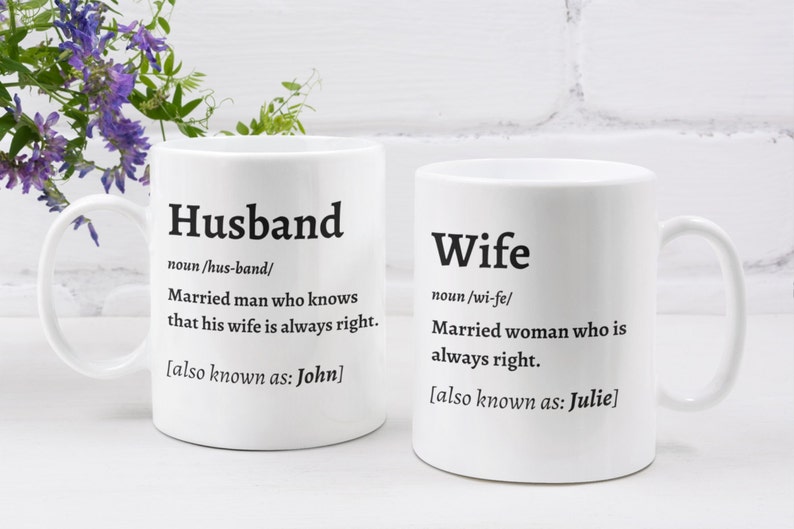 May include: Two white ceramic mugs with black text. One mug says "Husband" with a definition and "also known as: John." The other mug says "Wife" with a definition and "also known as: Julie."