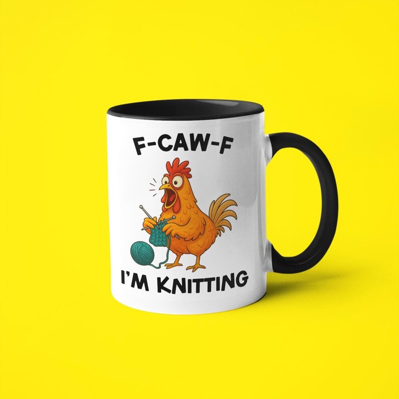 May include: White ceramic mug with a black interior and handle. The mug features a cartoon chicken knitting with the text "F-CAW-F I'M KNITTING". The background is a solid yellow.