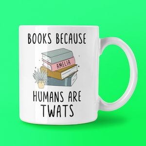 May include: White ceramic mug with a black handle. The mug features the text "BOOKS BECAUSE HUMANS ARE TWATS", a stack of books, and a small potted plant. One book is labelled "AMELIA".