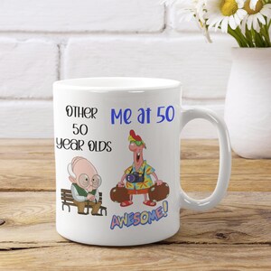 May include: White ceramic mug with the text "Other 50 Year Olds" and "Me at 50". The mug features cartoon illustrations of an elderly man and a man with luggage. The word "AWESOME!" is also on the mug.