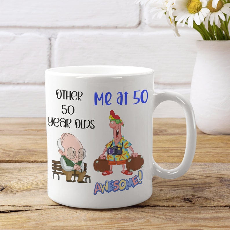 May include: White ceramic mug with the text "Other 50 Year Olds" and "Me at 50". The mug features cartoon illustrations of an elderly man and a man with luggage. The word "AWESOME!" is also on the mug.