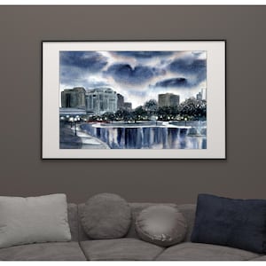 May include: A framed watercolor painting depicting a city skyline at dusk with a dark, cloudy sky above a calm body of water. The scene features silhouetted trees, illuminated street lamps, and tall buildings reflected in the water's surface.