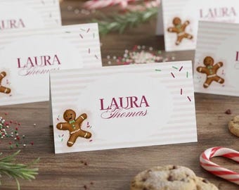 May include: Christmas-themed place cards with the name "Laura Thomas" in burgundy script. Each card features a gingerbread man illustration and decorative sprinkles. Cookies and a candy cane are also visible.