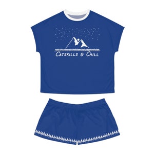May include: A blue pajama set with a white graphic of mountains and stars. The top has a white trim and the text "CATSKILLS & CHILL". The shorts have a white trim with a row of trees at the bottom.