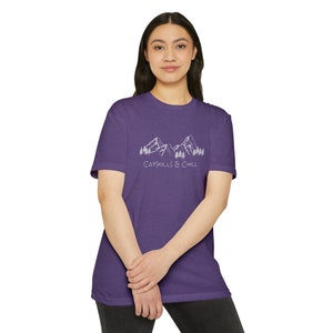 May include: Purple short-sleeved t-shirt with a white graphic of mountains and trees. The text "Catskills & Chill" is printed below the graphic.