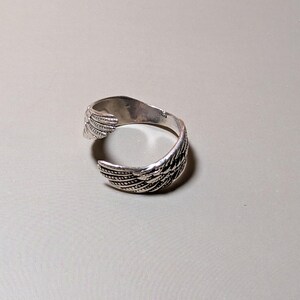 May include: A silver-toned cuff bracelet with a wing design. The open cuff features detailed feather patterns, creating a textured appearance. The bracelet is designed to wrap around the wrist.