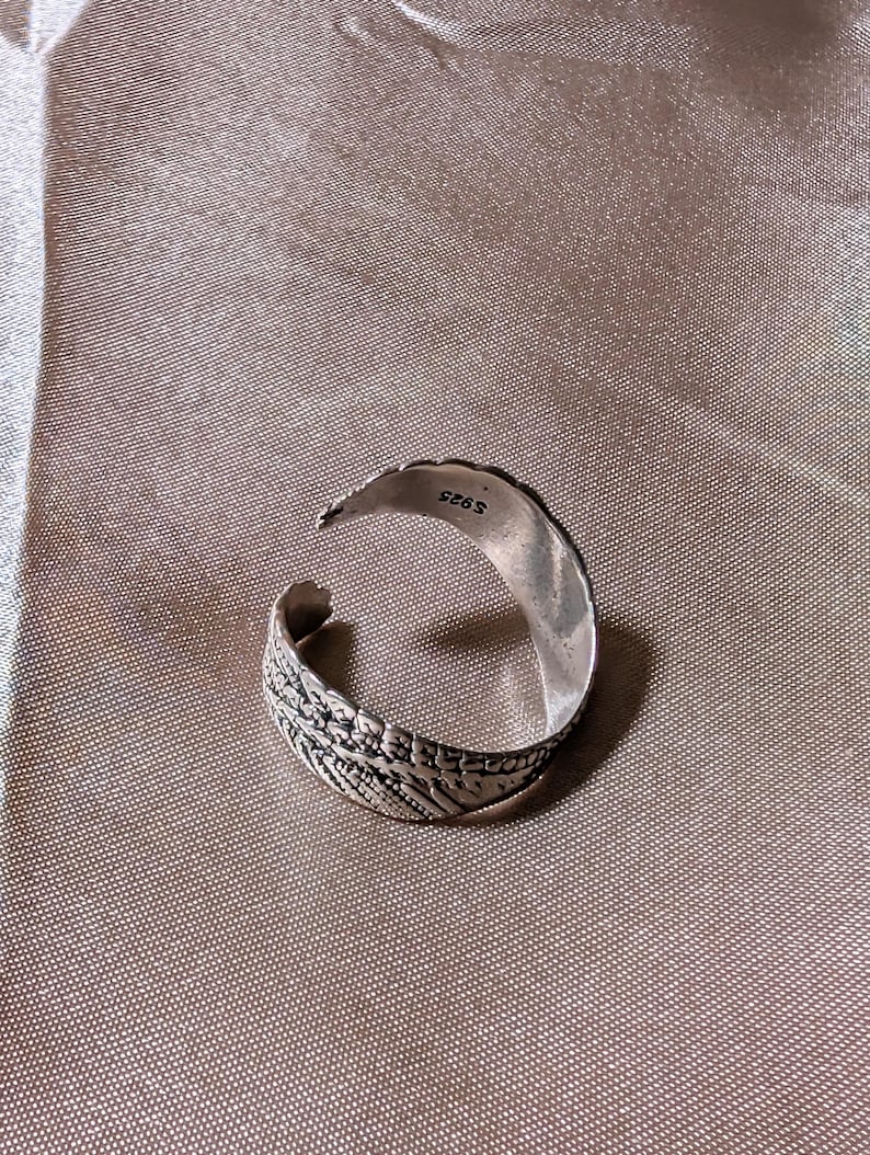 May include: A silver-colored adjustable ring with an open design. The ring features an intricate leaf pattern on the band and is stamped with "S925". The ring is set against a neutral background.