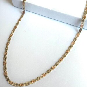Op de afbeelding: Een goudkleurige ketting met een delicaat kettingontwerp. De ketting heeft afwisselende secties van goud, ros&eacute;goud en zilverkleurig metaal, waardoor een driekleurig effect ontstaat. De ketting wordt gepresenteerd op een witte ondergrond.