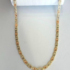 Op de afbeelding: Een goudkleurige ketting met een herhalend patroon van stervormige elementen en ovale schakels. De ketting heeft een driekleurig ontwerp, met goud-, ros&eacute;goud- en zilvertinten. De ketting wordt gepresenteerd tegen een witte achtergrond.
