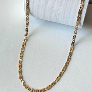 Op de afbeelding: Een goudkleurige ketting met een herhalend ovaal schakelontwerp. De schakels wisselen af tussen goud-, ros&eacute;goud- en zilverkleurige tinten, waardoor een veelkleurig effect ontstaat. De ketting wordt gepresenteerd tegen een witte achtergrond.