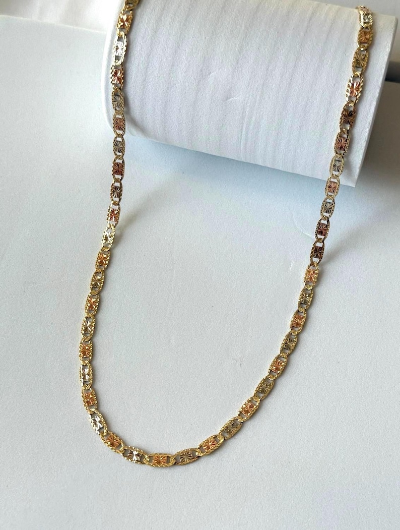 Op de afbeelding: Een goudkleurige ketting met een herhalend ovaal schakelontwerp. De schakels wisselen af tussen goud-, ros&eacute;goud- en zilverkleurige tinten, waardoor een veelkleurig effect ontstaat. De ketting wordt gepresenteerd tegen een witte achtergrond.