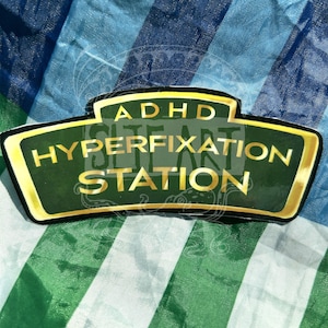 May include: A green and gold sticker with the text "ADHD Hyperfixation Station".