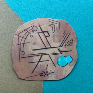 Puede incluir: Un recorte de papel irregular de color tostado con dibujos de tinta negra de formas geométricas, ángulos y pequeños puntos. Un elemento circular de color turquesa brillante está fijado en la parte inferior derecha.