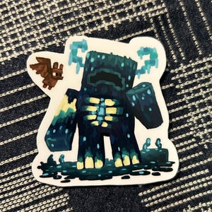 May include: A sticker featuring a stylized Warden character from the video game Minecraft. The Warden is depicted in dark blue and teal with yellow accents, surrounded by a dark blue and black background. A small brown bat is also included.