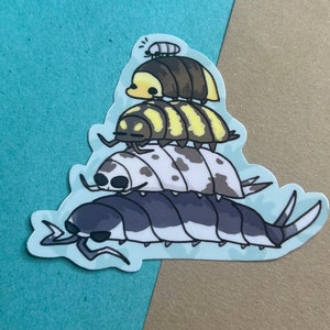 Puede incluir: Una pila de cuatro cochinillas de dibujos animados, cada una con un color y un patrón diferente. La cochinilla de abajo es negra y blanca, la segunda es blanca con manchas negras, la tercera es amarilla y negra a rayas, y la de arriba es marrón con una cabeza amarilla.