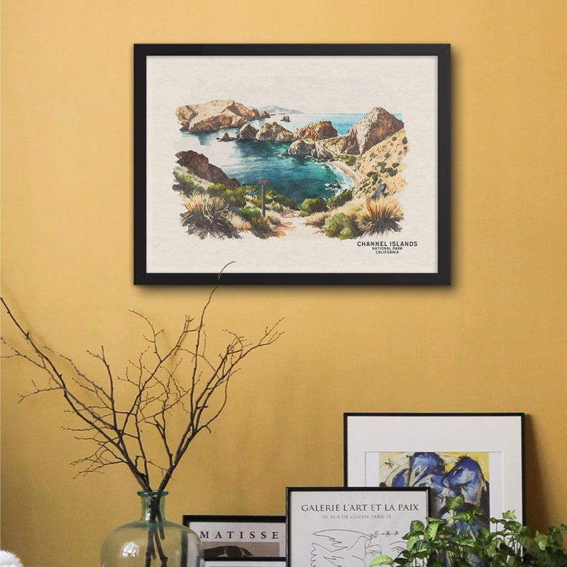 以下が含まれることがあります： カリフォルニア州チャネル諸島国立公園の入り江の風景を描いた、額縁に入った水彩画。絵画は、ターコイズブルーの海と展望台へのハイキングコースのある岩だらけの海岸線を描いています。