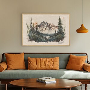Large framed Mount Rainier wall art print hanging above a mid-century modern green couch with orange pillows. Large scale PNW living room wall decor.