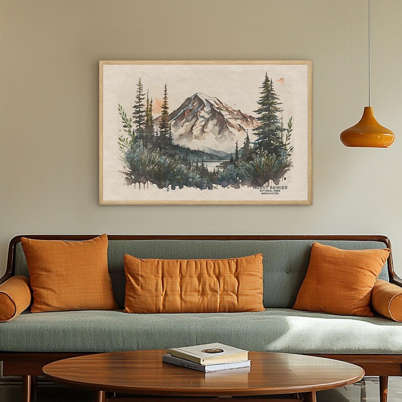 Large framed Mount Rainier wall art print hanging above a mid-century modern green couch with orange pillows. Large scale PNW living room wall decor.