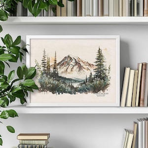 White framed Washington state Mount Rainier poster sitting on a white bookshelf, surrounded by stacked books and trailing green house plants. Nature inspired shelf decor.