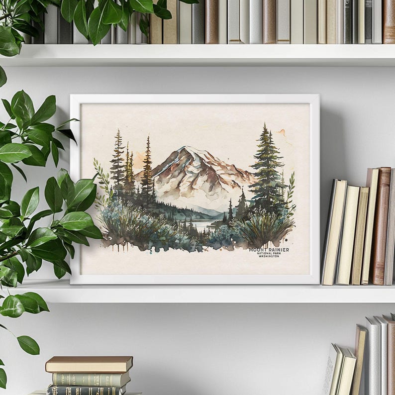 White framed Washington state Mount Rainier poster sitting on a white bookshelf, surrounded by stacked books and trailing green house plants. Nature inspired shelf decor.
