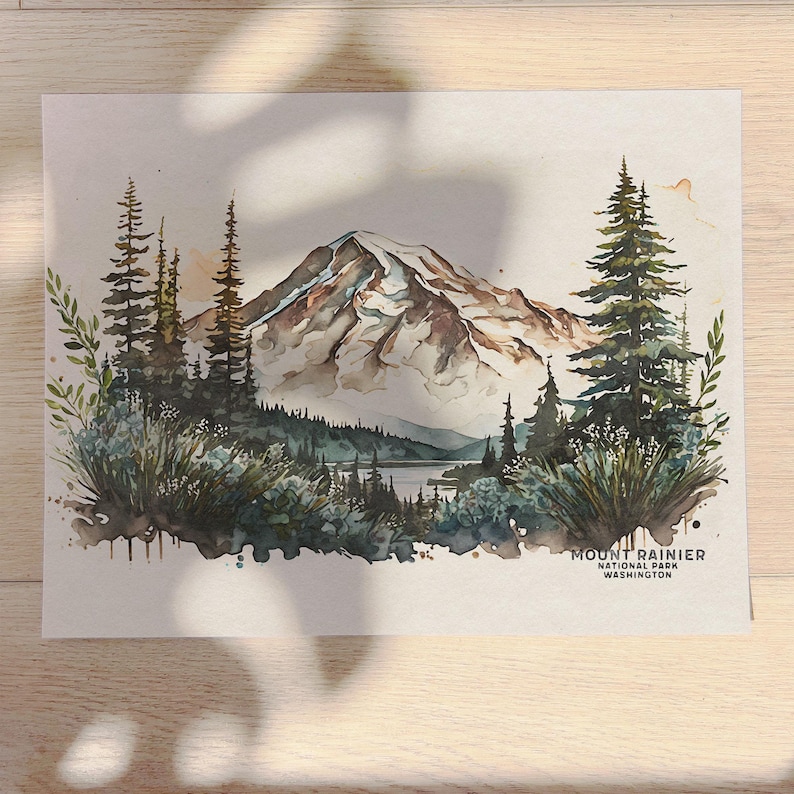 Close up of an unframed Mount Rainier National Park watercolor painting poster on a wooden desk, illuminated by natural sunlight and dappled leaf shadows.