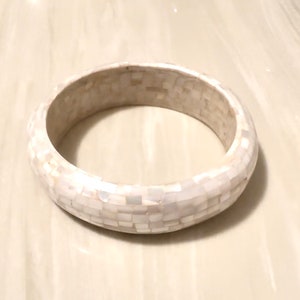 Puede incluir: Un brazalete blanco en forma de bangle hecho de pequeñas piezas cuadradas de nácar.