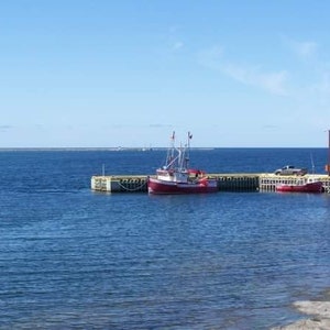 May include: A red fishing boat docked at a pier with a blue sky and calm water in the background.