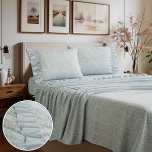 May include: Light blue floral patterned bed sheets and pillowcases. The bedding set features a ruffled edge on the pillowcases and the top sheet. The sheets have a delicate white floral pattern. The bed is made up with the sheets and pillowcases.
