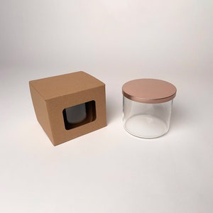 May include: A clear glass candle jar with a rose gold lid and a cardboard box with a window to display the jar.