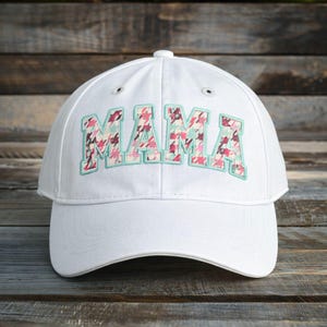 May include: A white baseball cap with the word "MAMA" embroidered across the front. The letters are filled with a pink, blue, and brown patterned fabric and outlined in light blue.