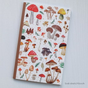 May include: A white sketchbook with a brown spine and a colorful mushroom pattern. The mushrooms are red, orange, yellow, brown, and white. The sketchbook is 5x8 inches.
