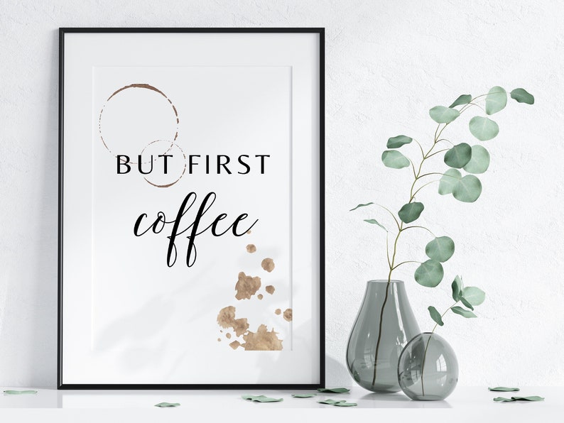 Puede incluir: Una impresi&oacute;n enmarcada con el texto "But first, coffee" en fuente de letra cursiva negra. La impresi&oacute;n presenta formas marrones parecidas a manchas de caf&eacute; sobre un fondo blanco.