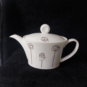 Könnte beinhalten: Weiße Teekanne mit braunem Wirbelmuster. Die Teekanne hat einen Deckel und einen Henkel.