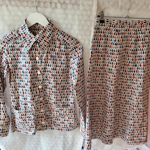 May include: A vintage two-piece outfit featuring a button-down shirt and a matching skirt. The set is patterned with a repeating teardrop design in shades of red, blue, brown, and white. The shirt has two front pockets and a collar.