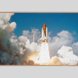 May include: A white and orange space shuttle launches into a blue sky with white clouds. The shuttle is surrounded by white smoke and fire.