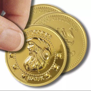 May include: Gold-coloured chocolate coins with embossed details. One coin features a bearded figure and the text "Gringotts Bank." Other coins display the words "Coco Chocolates" and bird illustrations. A hand is holding one of the coins.