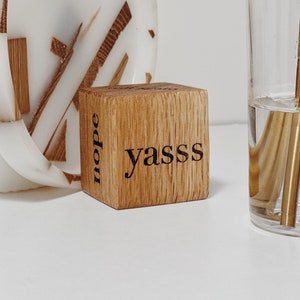 May include: A wooden block with the words "dope" and "yass" engraved on it. The block is sitting on a white surface.