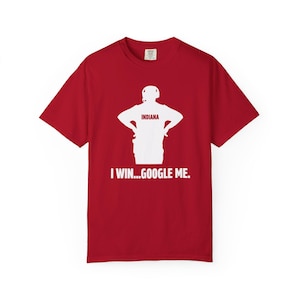 May include: Red t-shirt with a white graphic of a person with the word "INDIANA" above the figure. The text "I WIN...GOOGLE ME." is printed below the graphic. The shirt is made of a soft material.