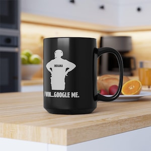 May include: Black ceramic mug with a white graphic of a person wearing a headset and the word "INDIANA" on the chest. The text "I WIN...GOOGLE ME." is printed below the graphic. The mug has a large handle.