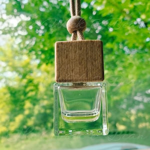 May include: A clear glass bottle with a wooden lid, hanging from a brown string. The bottle is filled with a clear liquid and is designed to be used as a car air freshener.