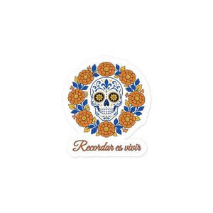 Peut inclure: Un autocollant découpé représentant un crâne blanc central avec des motifs décoratifs bleus et jaunes, entouré d'une couronne circulaire de fleurs de souci orange et de feuilles bleues, avec le texte Recordar es vivir en dessous.